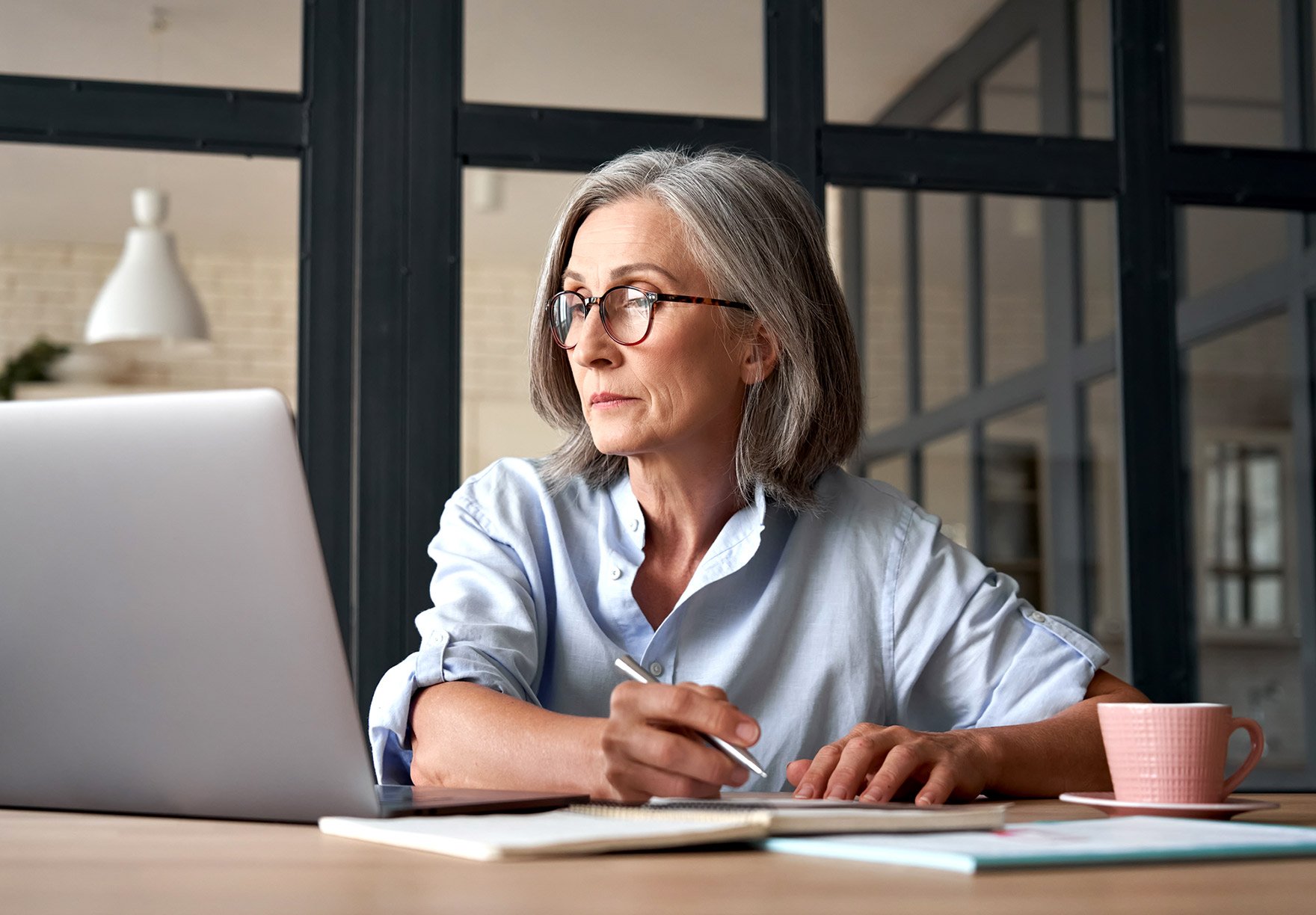 Woman reviewing W-8 BEN forms and taking notes while referencing records on her laptop. 